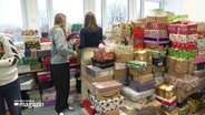 Zwei Schülerinnen stehen inmitten von sehr vielen Geschenkpaketen. © Screenshot 