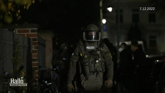 Die Polizei beim Transport des Verdächtigen, im Zentrum des Bildes ein Polizist in dicker Montur. © Screenshot 