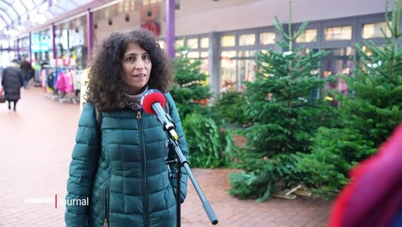 Eine Frau im Interview, im Hintergrund ein Stand mit Weihnachtsbäumen. © Screenshot 