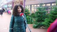 Eine Frau im Interview, im Hintergrund ein Stand mit Weihnachtsbäumen. © Screenshot 