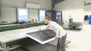 Ein Handwerker bereitet Ambiena-Heizplatte auf einer Werkbank vor. Eine dünne Platte mit dunkler Oberfläche und weißem Rand. © Screenshot 