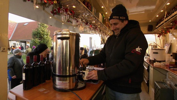 Ein Mann steht hinter einem tresen und zapft Glühwein. © Screenshot 