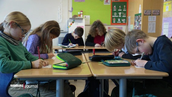 Das Foto zeigt sechs Grundschüler:innen, die in ihrem Klassenzimmer konzentriert an den Weihnachtskarten schreiben. © Screenshot 