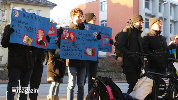 Das Foto zeigt sieben der demonstrierenden Studierenden mit gebastelten Plakaten. © Screenshot 