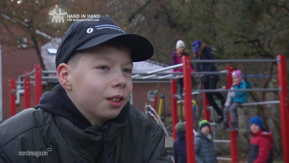 Ein Junge im Interview, im Hintergrund andere Kinder auf einem Klettergerüst. © Screenshot 