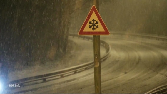 Das Foto zeigt eine Straße bei Nacht. Es schneit. Im Fokus des Bildes warnt ein Schild vor der Witterung. © Screenshot 
