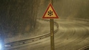 Das Foto zeigt eine Straße bei Nacht. Es schneit. Im Fokus des Bildes warnt ein Schild vor der Witterung. © Screenshot 