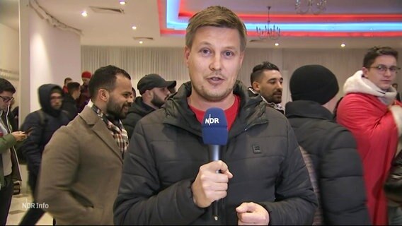NDR-Reporter Sebastian Rieck berichtet von einer Marokko-Fanparty in Billstedt. Im Vordergrund ist der Journalist, im Hintergrund einige Fans zu sehen. © Screenshot 