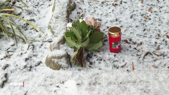 Ein Blumenstrauß und eine Kerze liegen im Schnee. © Screenshot 