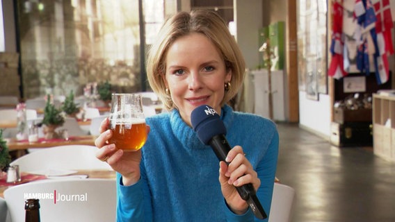 Julia Wulf hält ein Glas Craftbeer und ein Mikrofon in den Händen. © Screenshot 