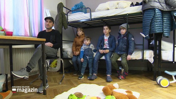 Ein Mann sitzt mit seinen vier Kindern in einer Flüchtlingsunterkunft. © Screenshot 