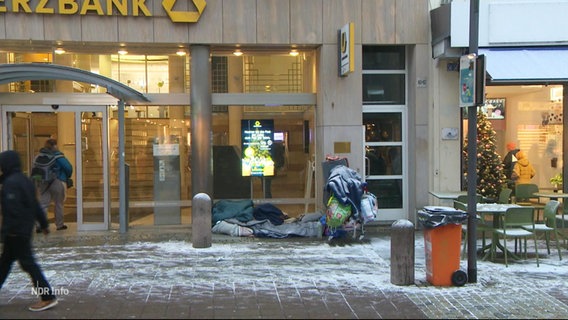 Ein Obdachloser hat sein Lager in einer verschneiten Einkaufsstraße aufgeschlagen. © Screenshot 
