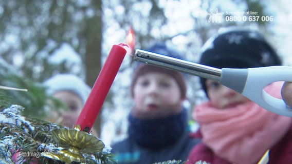 Eine Kerze auf einem Tannenbaum vor Kindern. © Screenshot 