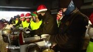 Helfer mit Weihnachtsmützen verteilen Essen an Obdachlose. © Screenshot 
