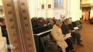 In einer Kirche sitzen Gemeindemitglieder in Decken bei einem Gottesdienst. Im Vordergrund: ein Thermometer zeigt eine Temperatur von -8°C. © Screenshot 