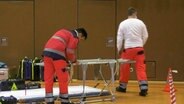 Rettungskräfte bauen eine improvisierte Anlaufstelle in einer Sporthalle auf. © Screenshot 