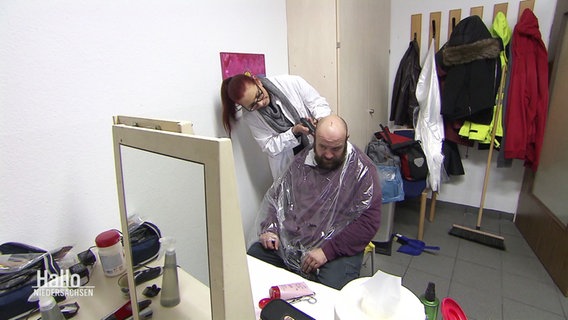 Eine Frau schneidet einem Mann mit Vollbart die Haare. © Screenshot 