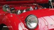 Nahaufnahme eines roten "Triumph" Oldtimers mit geöffneter Motorhaube. © Screenshot 