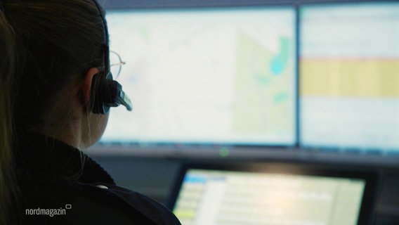 Eine Polizeibeamtin mit Headset telefoniert vor einem Bildschirm in einer Einsatzleitstelle. © Screenshot 