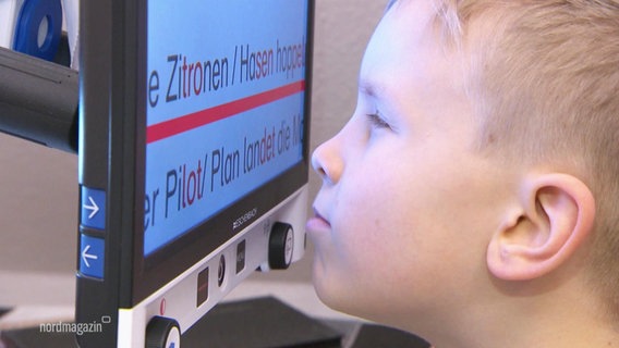 Ein kleiner Junge sitzt einige Zentimeter vor einem Bildschirm mit zugekniffenen Augen und versucht die vergößerte Schrift darauf zu lesen. © Screenshot 