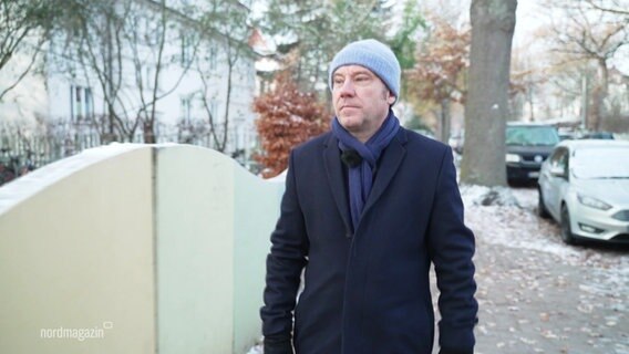 Autor Gregor Sanders trägt Mantel, Mütze und Schal und geht durch eine etwas verschneite Straße in eienr Wohngegend. © Screenshot 
