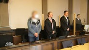 Ein Verdächtiger und seine Anwälte stehen in einem Gerichtsaal © Screenshot 