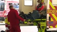 Ein Patient wird auf einer Liege von zwei Personen des Rettungssanitätspersonals aus einem Rettungswagen geschoben. © Screenshot 