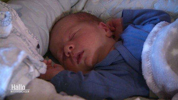 Ein Säugling liegt friedlich mit geschlossenen Augen in einer Decke. © Screenshot 