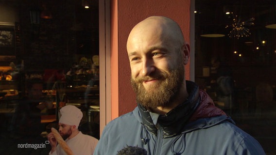Ein Mann mit Glatze und Vollbart lächelt bei einer Straßenumfrage in die Kamera. © Screenshot 