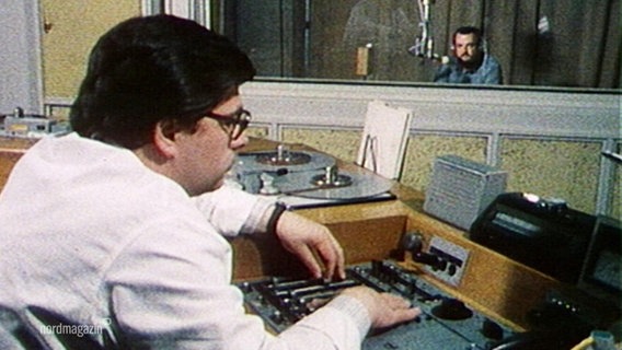 Eine Person sitzt vor einem Tonbandgerät, im Hintergrund sitzt jemand in einem Studio © Screenshot 