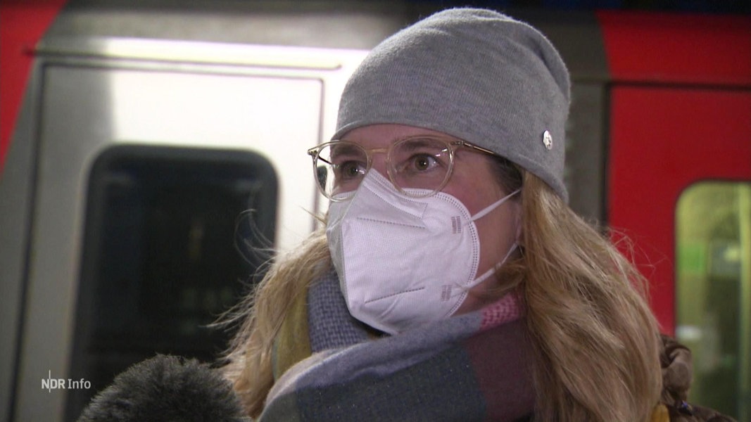 Eine Frau, vor einer S-Bahn stehend, trägt eine Maske.