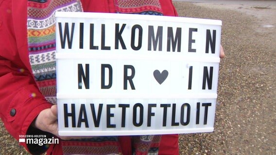 Ein Schild mit der Aufschrift: "WILLKOMMEN NDR IN HAVETOFTLOIT" wird gehalten. © Screenshot 
