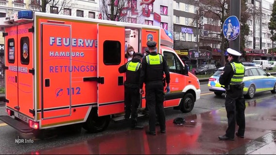 Polizeibeamte stehen bei einem Rettungswagen © Screenshot 