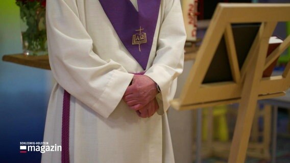 Im Anschnitt sind das Gewand und die Hände eines christlichen Geistlichen zu sehen. © Screenshot 