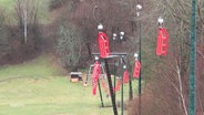 Rote Schlitten hängen an einem unbenutzten Skilift über grünen Wiesen. © Screenshot 