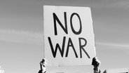 Hände halten ein Schild mit der Aufschrift NO WAR hoch. © Screenshot 