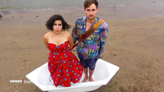 Ausschnitt aus einem Musikvideo: Hêja Netirk (li.) und einer ihrer Bandkollegen stehen in einer Badewanne am Hamburger Elbstrand. © Screenshot 