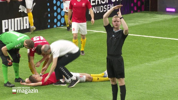 Jannek Hansen (ganz re.) als Schiedsrichter bei einem Hallenfußball-Spiel. Er gibt das Zeichen für ein Time-out, weil ein Spieler sich verletzt hat. © Screenshot 