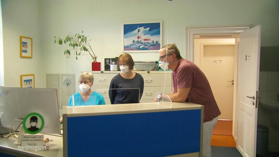 Drei Personen stehen am Empfangstresen einer Hausarztpraxis. © Screenshot 