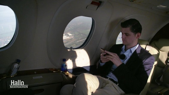 In der Kabine eines kleinen Passagierflugzeugs sitzt ein Mann am Fenster und schaut auf sein Smartphone. © Screenshot 