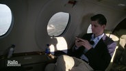 In der Kabine eines kleinen Passagierflugzeugs sitzt ein Mann am Fenster und schaut auf sein Smartphone. © Screenshot 