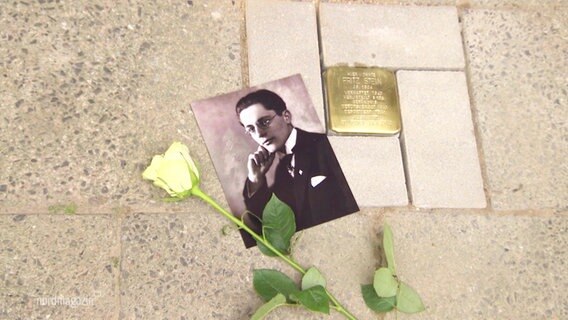 Ein Stolperstein für den jüdischen Mann Fritz Stein, der in der NS-Zeit von den Nationalsozialisten ermordet wurde. Daneben ein Schwarzweiß-Foto und eine gelbe Rose. © Screenshot 