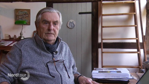 Krimiautor Rolf Dieckmann sitzt am Schreibtisch und blickt in die Kamera. © Screenshot 