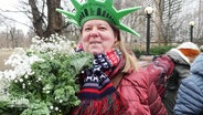 Eine Teilnehmerin der Grünkohlfahrt nach New York mit grünem Strauß und Freiheitsstatue-Kopfschmuck. © Screenshot 