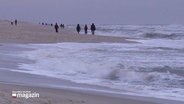 Die Urlauber auf Sylt lassen sich auch von Wind und Wetter nicht abschrecken und gehen am Strand spazieren. © Screenshot 