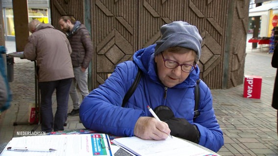 Eine Frau unterschreibt auf einem Klemmbrett © Screenshot 