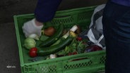 Eine Person packt Gemüse in eine grüne Plastikbox. © Screenshot 