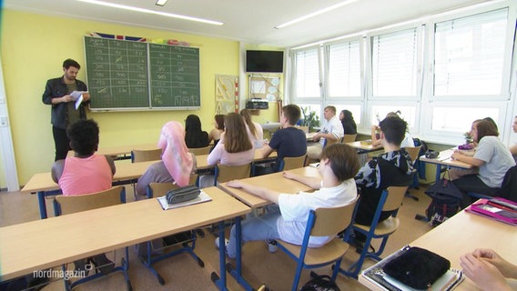 Ein Lehrer steht vor Schülerinnen und Schülern in einem Klassenraum. © Screenshot 