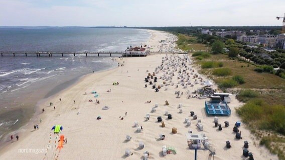 Ein Strand voller Strandkörbe und mit einer Seebrücke aus der Vogelperspektive. © Screenshot 