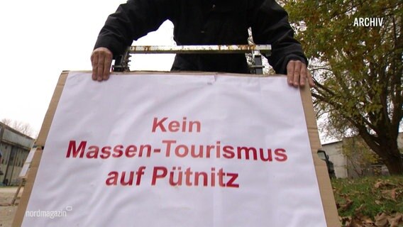 Eine Person hält ein Schild mit der Aufschrift: Kein Massentourismus auf Pütnitz. © Screenshot 